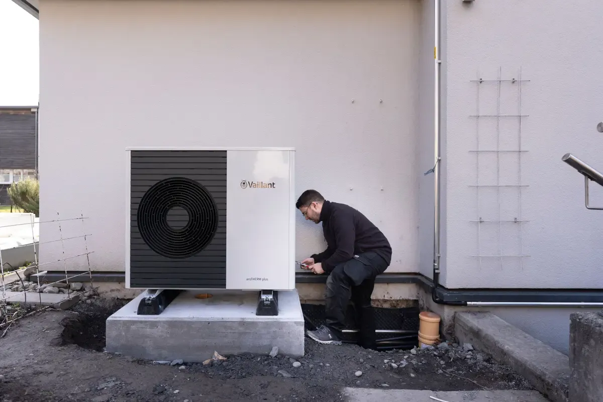 Ein Installateur verbindet die Rohre, die vom Keller kommen, mit der Wärmepumpe, die sich hinter dem Haus befindet (Mels, Sankt Gallen).