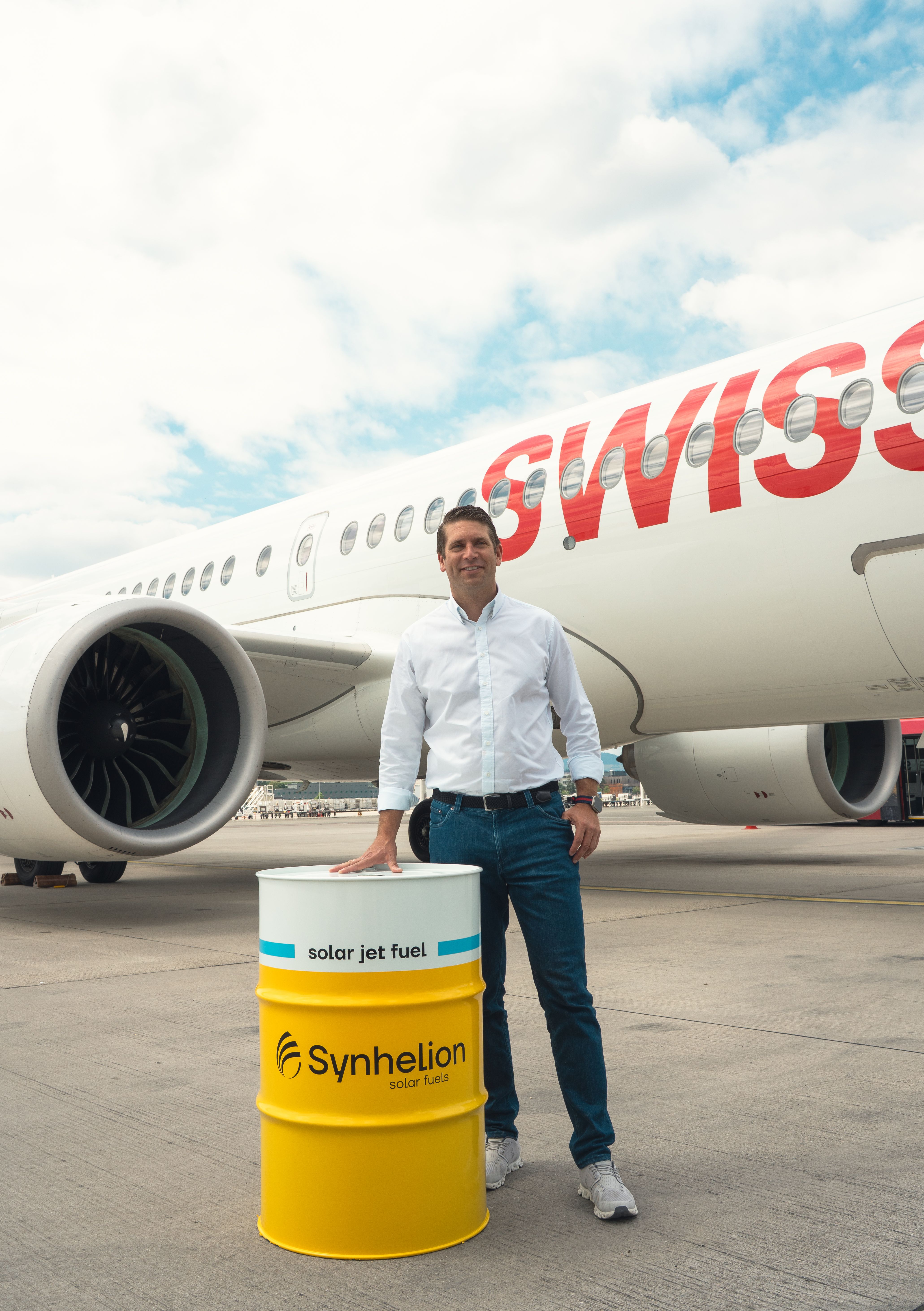 Philipp Furler, Co-CEO von Synhelion, steht auf dem Rollfeld vor einem SWISS-Passagierflugzeug neben einem gelben Fass mit der Aufschrift «Synhelion – solar jet fuel».