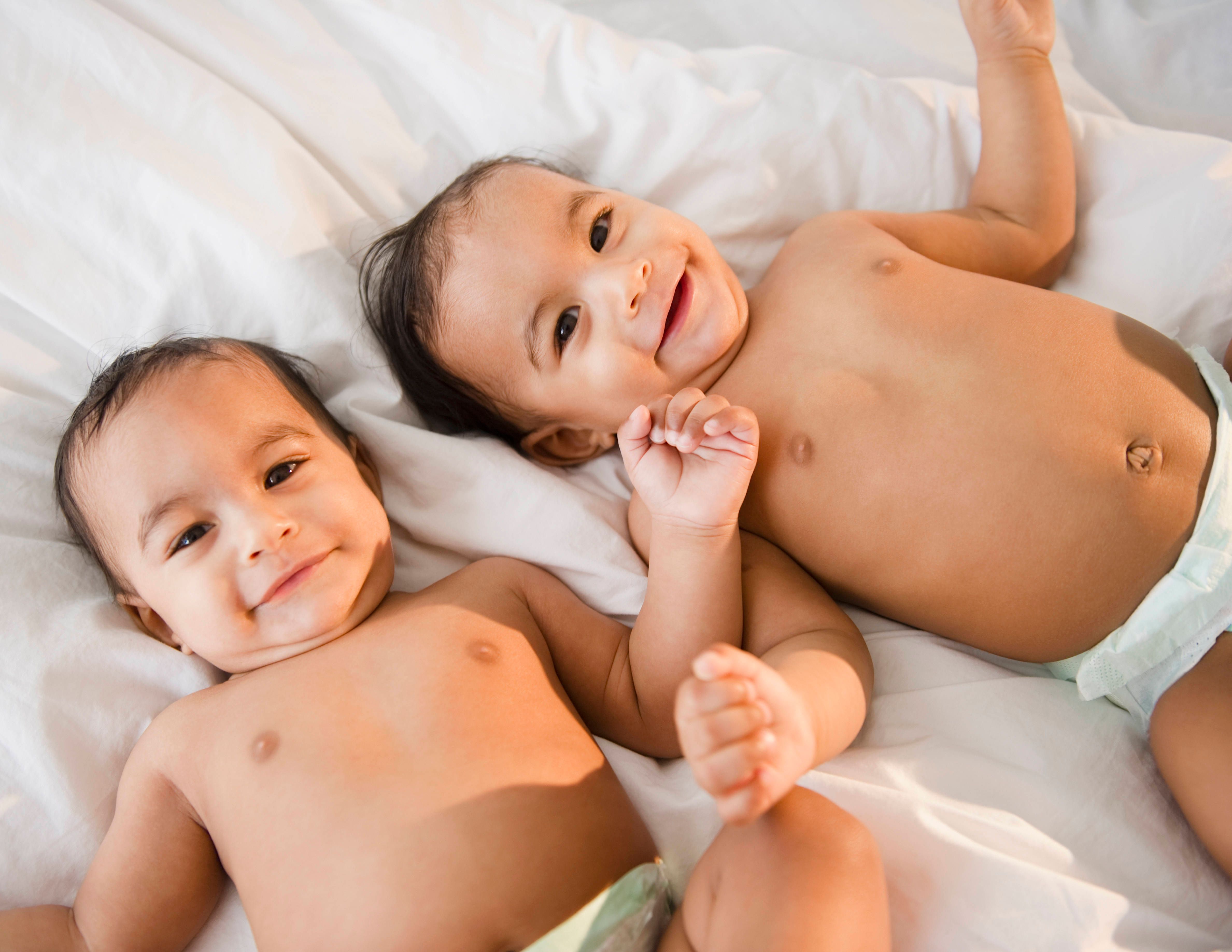 Mixed race twins in diapers laying on bed
