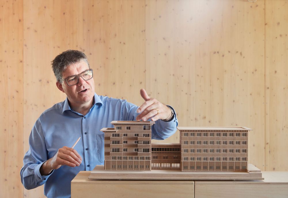 Pirmin Jung erläutert an einem Architekturmodell das Büro- und Wohnhaus «Haus des Holzes» in Sursee; Innenaufnahme vor holzverkleideter Wand.