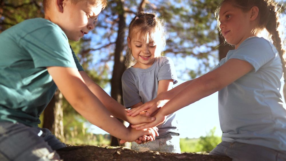 Trois enfants se tiennent debout dans une forêt et joignent leurs mains, en signe d'esprit d'équipe et de jeu collectif.