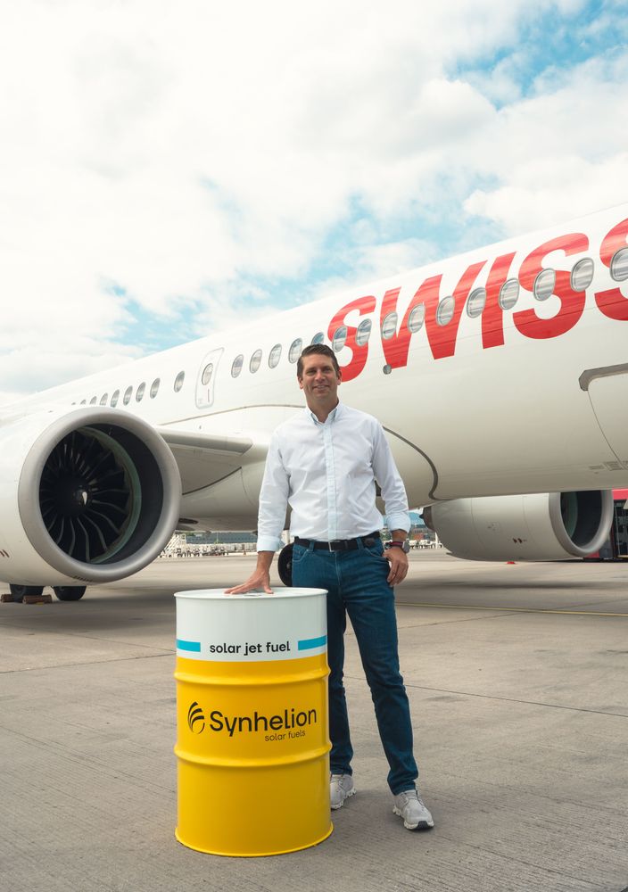Philipp Furler, Co-CEO von Synhelion, steht auf dem Rollfeld vor einem SWISS-Passagierflugzeug neben einem gelben Fass mit der Aufschrift «Synhelion – solar jet fuel».