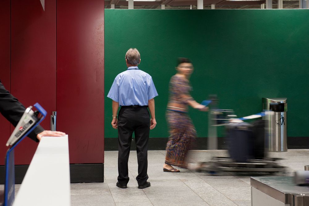 Une femme passe devant un douanier à l'aéroport de Zurich avec un chariot à bagages