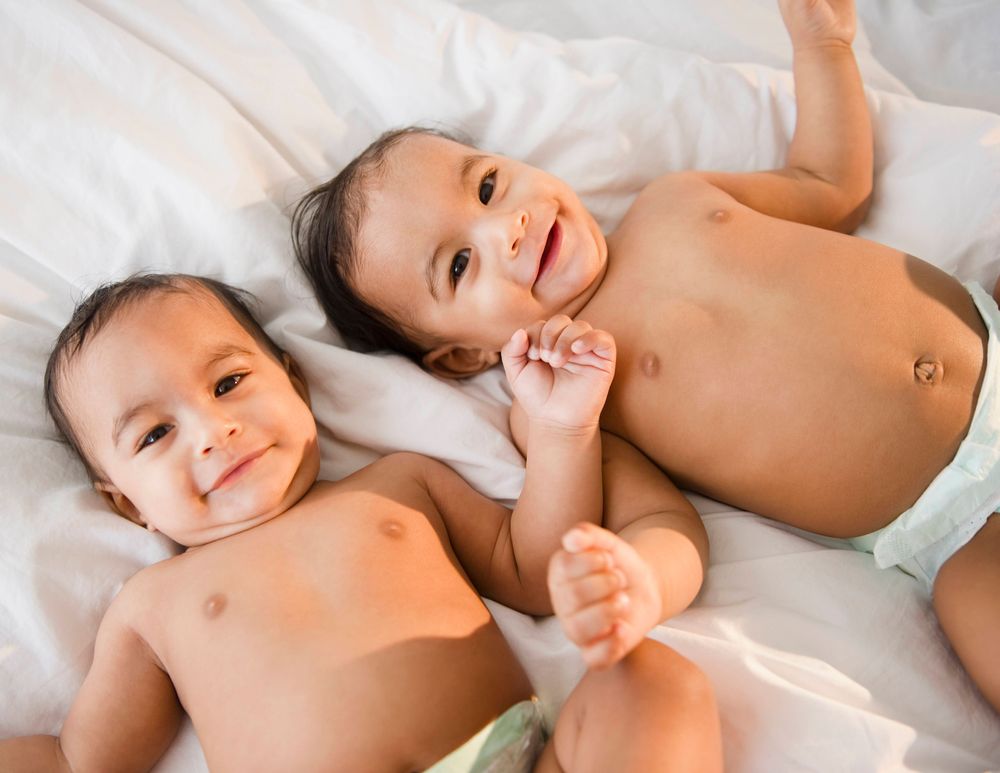 Mixed race twins in diapers laying on bed