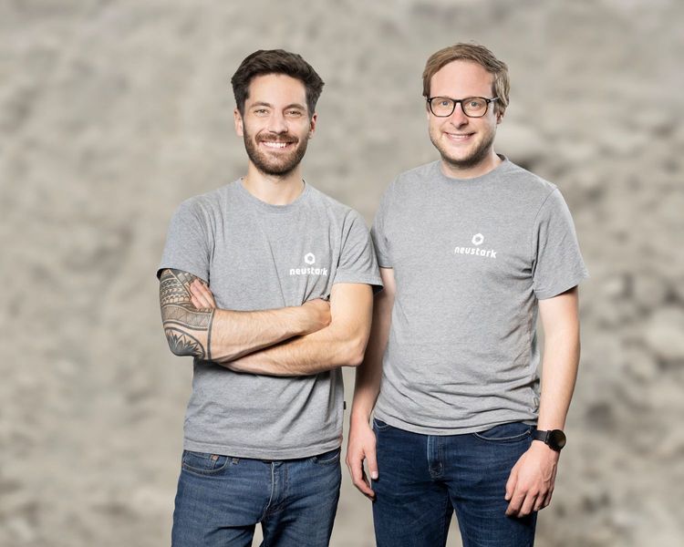 Les cofondateurs de neustark, Valentin Gutknecht et Johannes Tiefenthaler, se tiennent côte à côte devant un fond neutre et portent des T-shirts gris avec le logo de neustark.