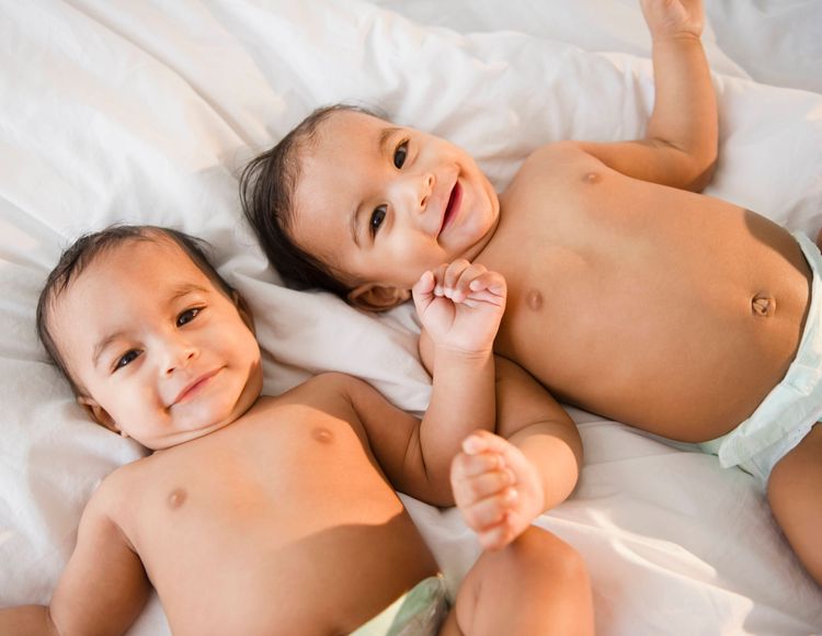 Mixed race twins in diapers laying on bed