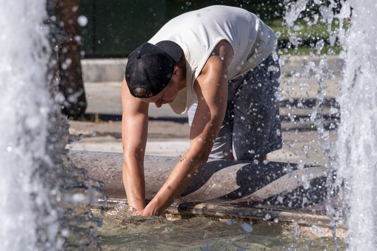 Ein Tourist kühlt sich an einem Hitzetag in Athen im Juli 2024 an einem Brunnen ab
