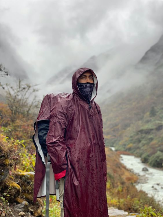 Ein Mann steht im Regen in einem Gebirge und trägt eine dunkelrote Regenjacke