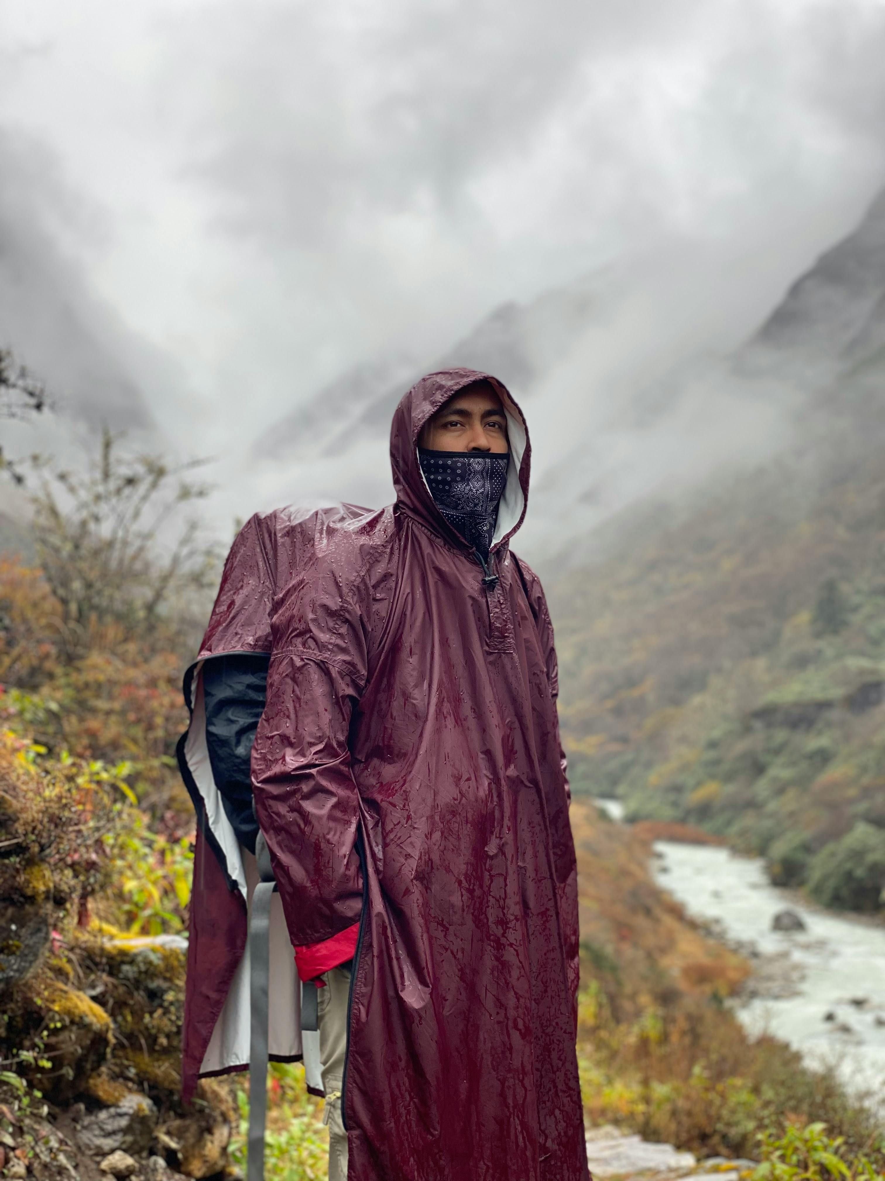 Ein Mann steht im Regen in einem Gebirge und trägt eine dunkelrote Regenjacke