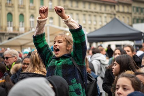 Jubelende junge Demonstrantin mit hochgereckten Armen inmitten einer Menschenmenge auf einer Kundgebung in der Stadt.