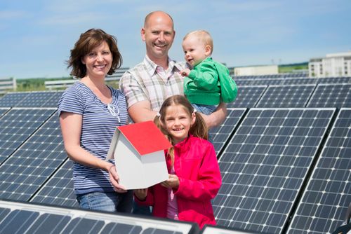 Eine Familie mit zwei Kindern steht neben einer Solaranlage für Privathäuser und hält ein kleines Haus in der Hand