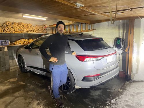 Gilles Roulin se tient à côté de sa voiture électrique, qui est rechargée avec la station de recharge de FMB dans le garage de sa maison de vacances.